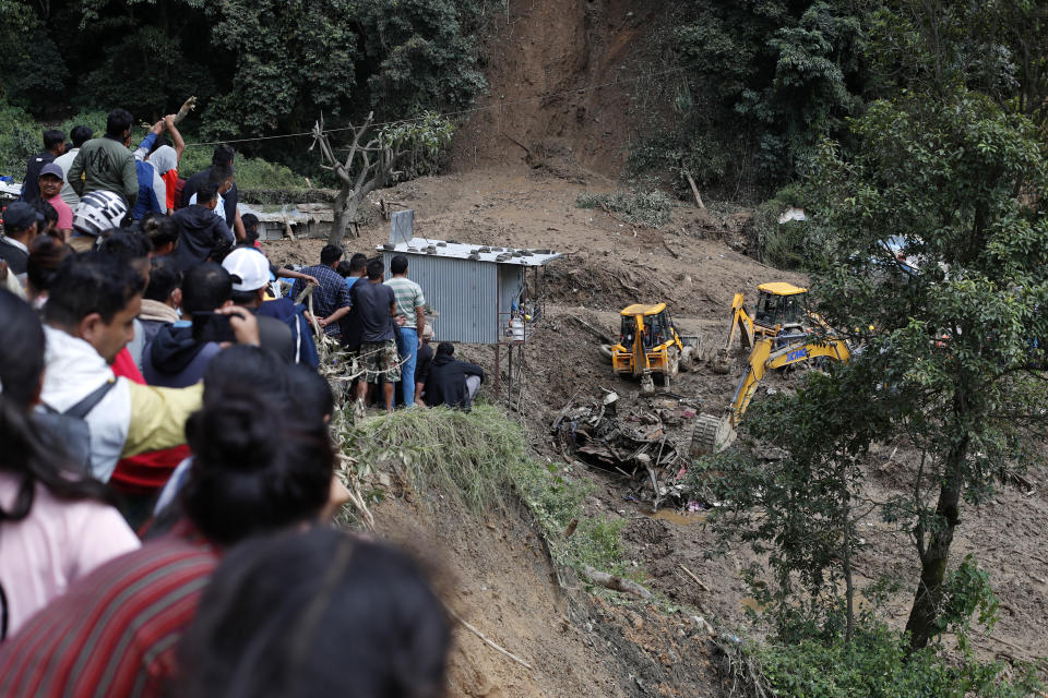 Gente mirando mientras varias topadoras sacan restos de autos y cuerpos de víctimas atrapadas por un alud de tierra provocado por aguaceros en Katmandú, Nepal, el domingo 29 de septiembre de 2024. (AP Foto/Sujan Gurung)