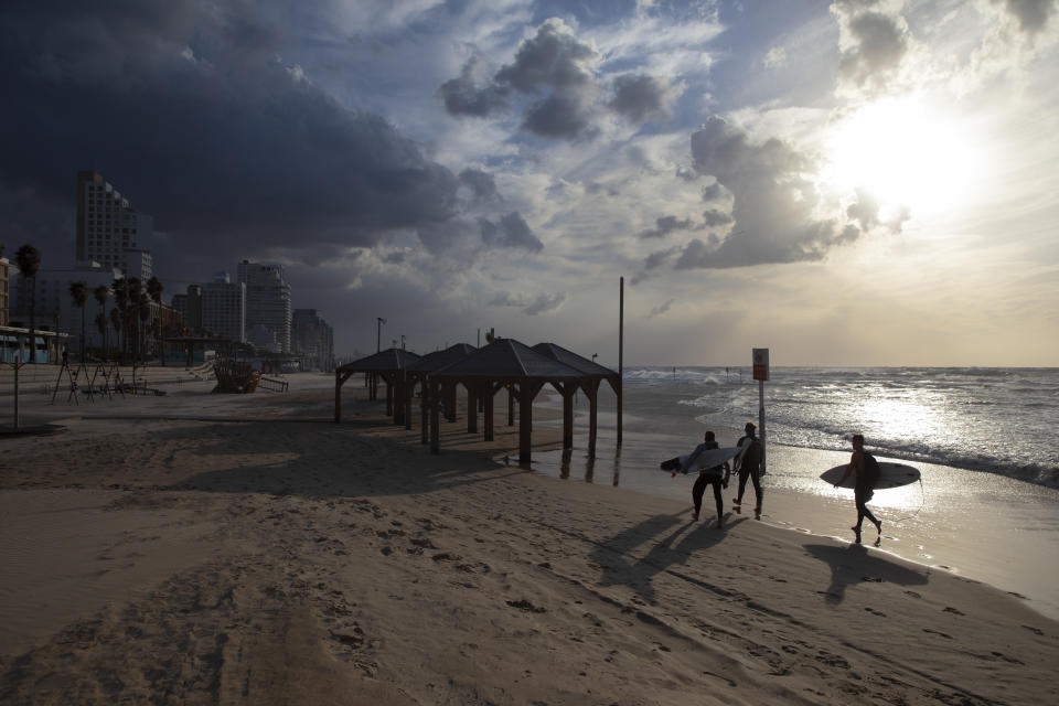 Surfers carry their boards along the beach front during a nationwide lockdown to curb the spread of the oronavirus, In Tel Aviv, Israel, Sunday, Jan. 17, 2021. (AP Photo/Oded Balilty)