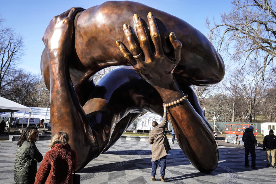 A man reaches to touch a detail of the 20-foot-high bronze sculpture 