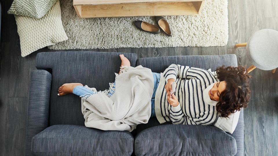 High angle shot of an attractive young woman using her cellphone while relaxing on a couch at home.