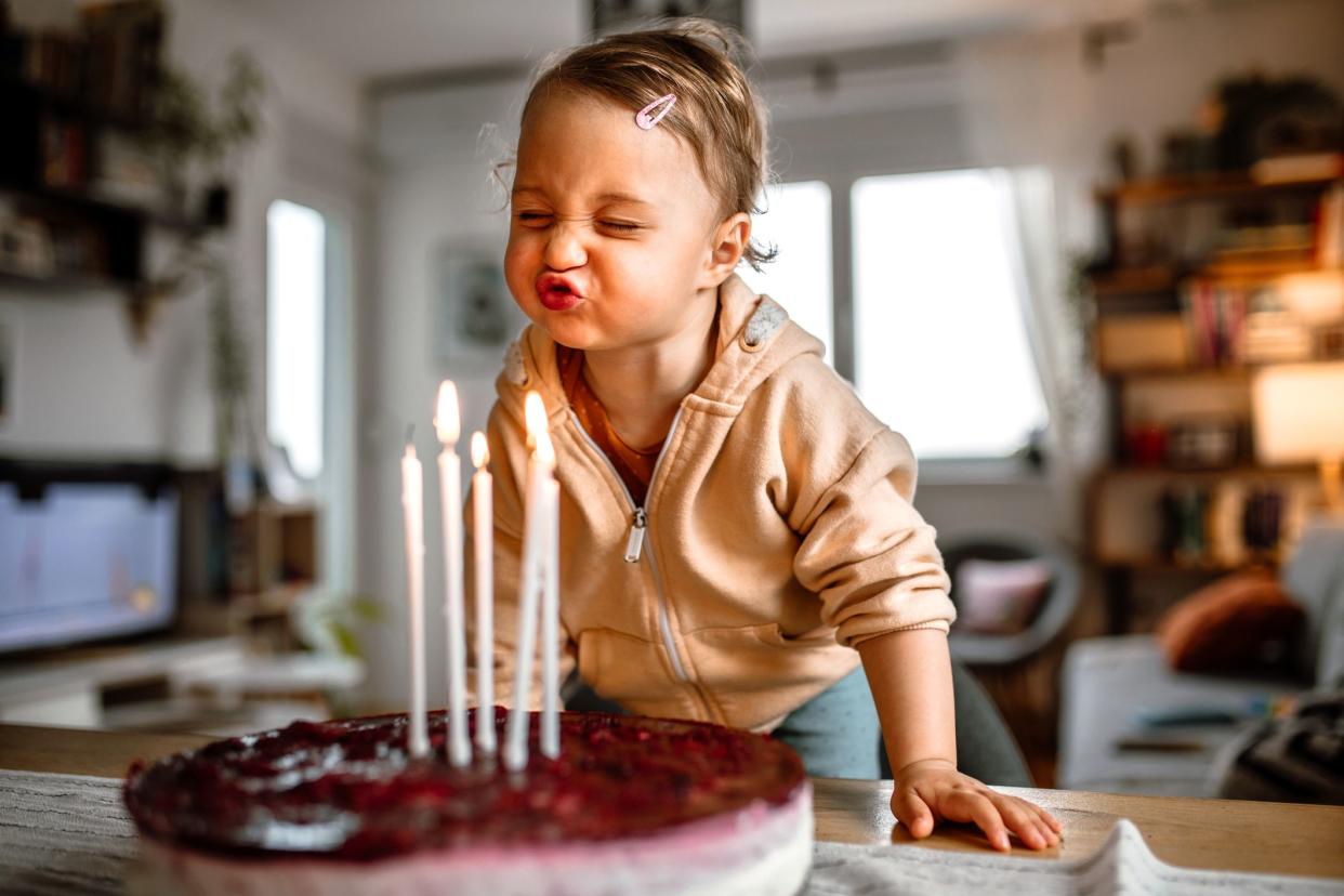 Little birthday girl blowing out candles on cake at home. Standing at the table and trying to blow out all candles on delicious cheesecake.