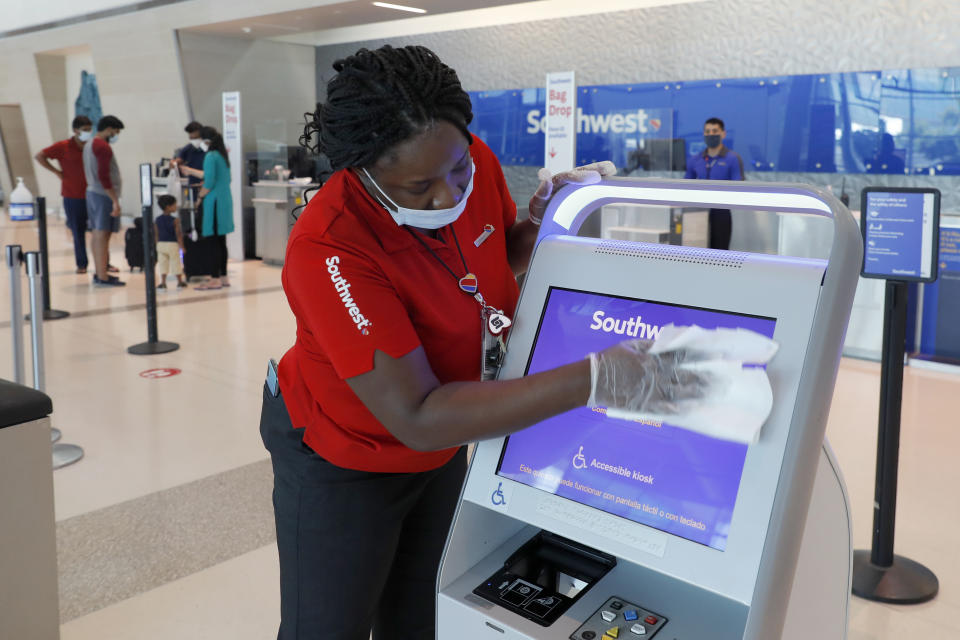 In this June 24, 2020, photo, Southwest Airlines employee, La Toya Malone Key wipes down a kiosk after it was used by a passenger to secure their boarding pass at Love Field in Dallas. (AP Photo/Tony Gutierrez, File)