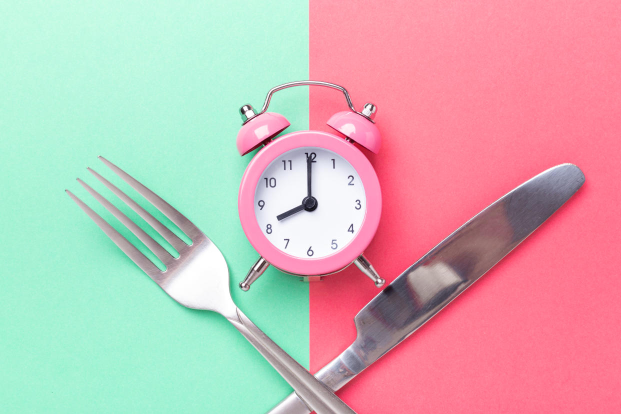 In a photo illustration, an alarm clock lies on its back between a crossed fork and butter knife.