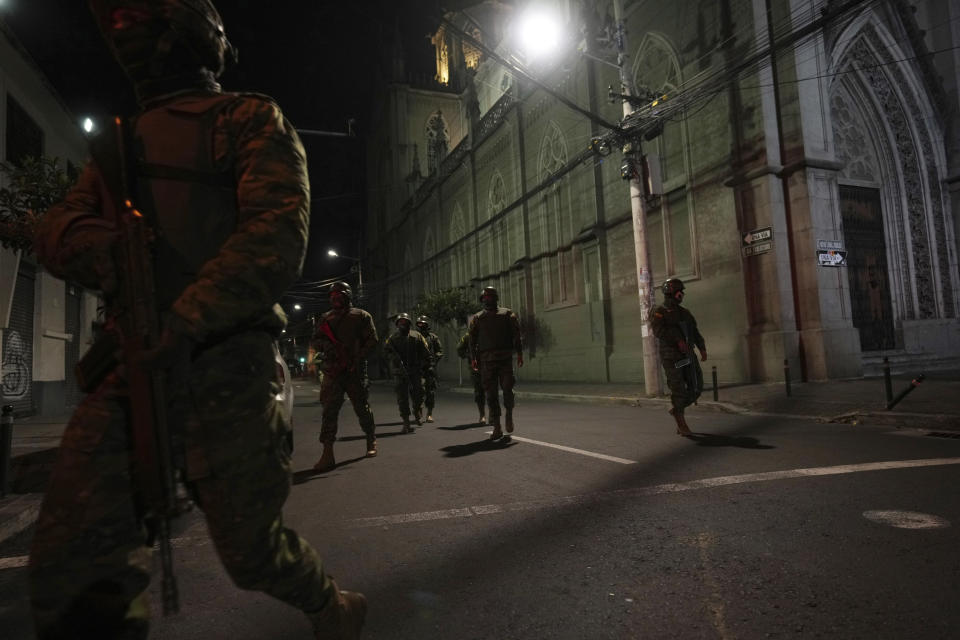 Soldiers walk towards a vehicle that blew up outside the Women´s and Human Rights Ministry building in Quito, Ecuador, late Wednesday, Aug. 30, 2023. The building used to be the location of the government’s National Service for Attention for People Deprived of Liberty (SNAI), which runs the jail system. (AP Photo/Dolores Ochoa)