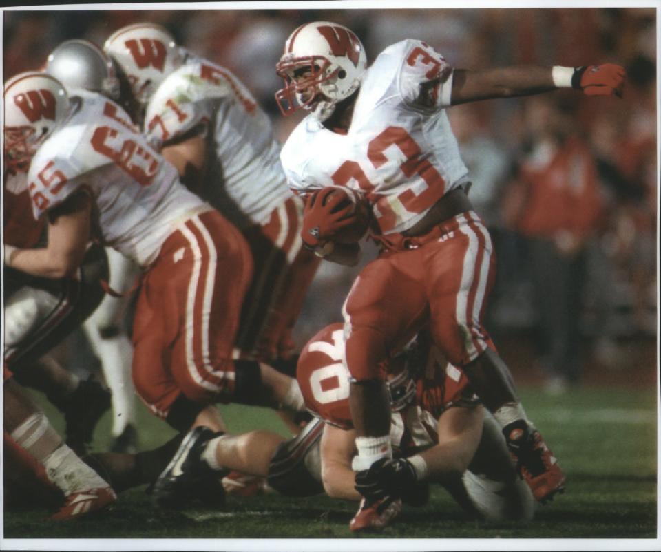 Wisconsin Badgers running back Brent Moss heads out behind his blockers but is grabbed around the ankle by Ohio State tackle Matt Bonhaus during a game in 1994. Moss died Sunday at age 50.