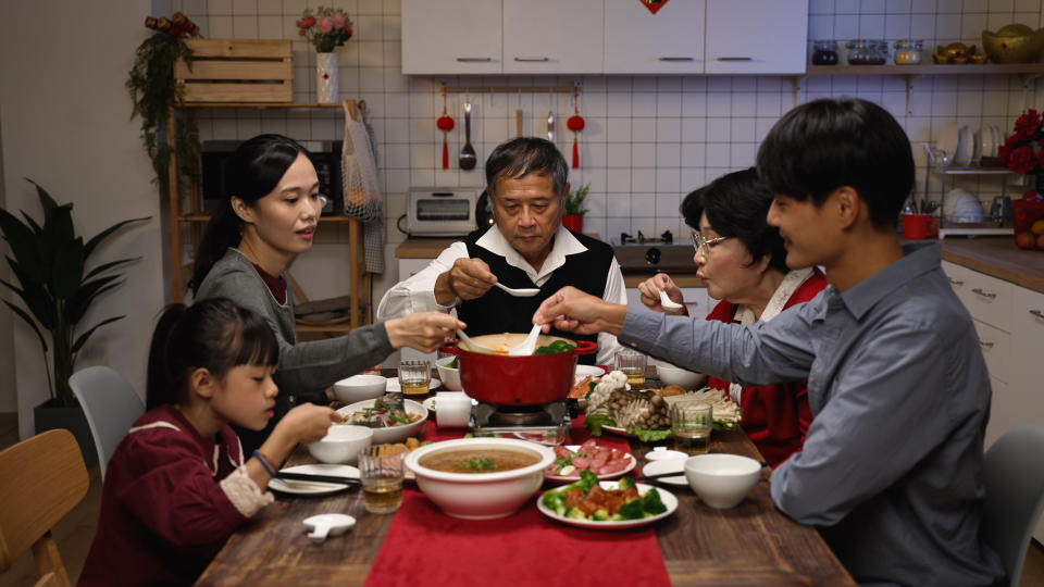 asian extended family blowing and tasting the hot delicious soup with spoons while they are gathering together for new year’s reunion meal at home in the evening