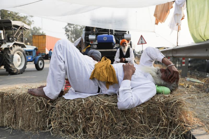 A farmer rests on a stack of hay at a site of a protest against the newly passed farm bills at Singhu border near Delhi