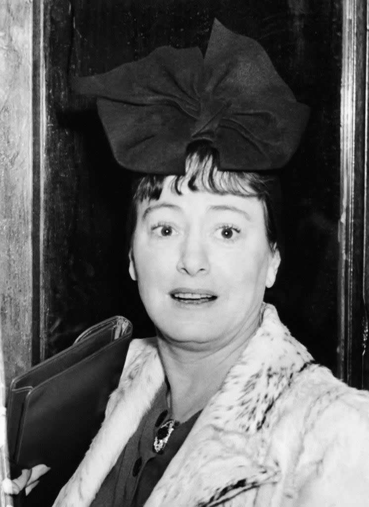 Dorothy Parker wearing a fur coat and a large bow hat, holding a clutch while looking surprised