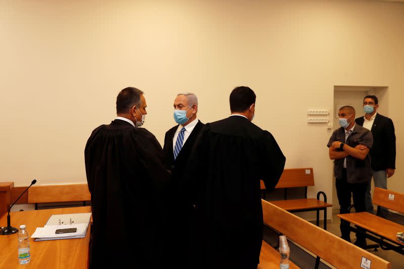 Israeli Prime Minister Benjamin Netanyahu, wearing a face mask, stands inside the court room as his corruption trial opens at the Jerusalem District Court