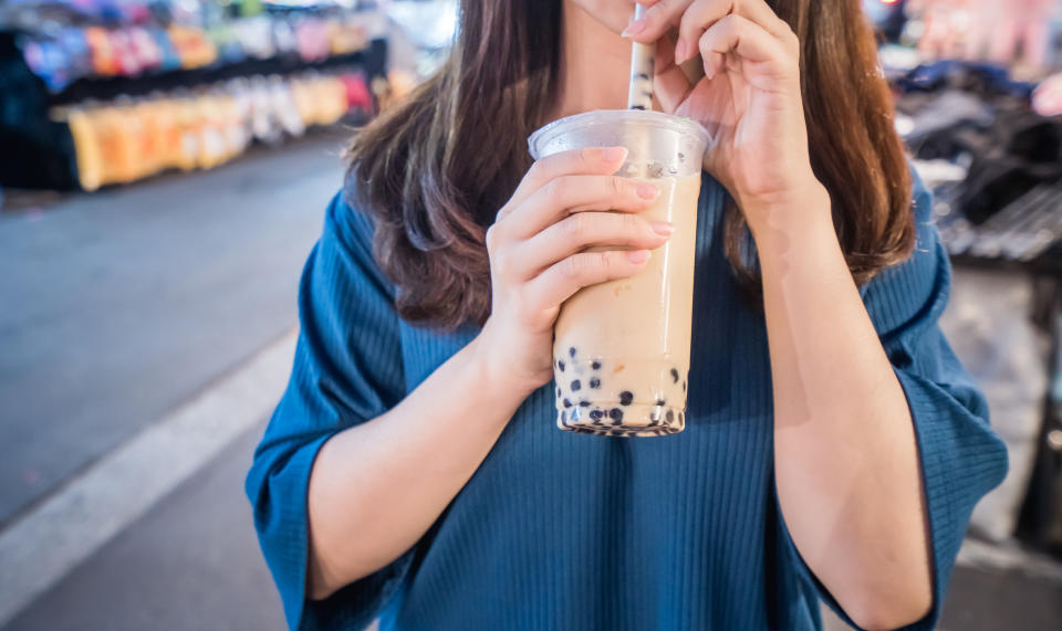 A young woman is drinking a plastic cup of bubble milk tea with a straw at a night market in Taiwan, Taiwan delicacy, close up.