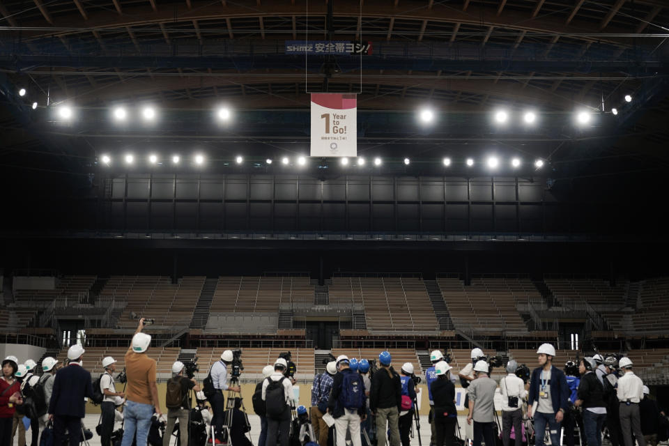 Members of the media gather near a "1-Year to Go" banner during a tour Monday, July 22, 2019, in Tokyo. Despite scandals, rising costs and doubts about the economic payoff, the Tokyo Olympics will be a must-see event — if you can find a ticket or a hotel room — when they open in a year. Tokyo was supposed to be a "safe pair of hands" after Rio de Janeiro's corruption and near-meltdown three years ago. (AP Photo/Jae C. Hong)