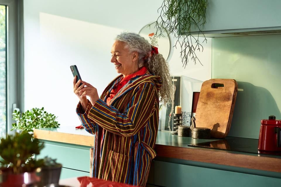 An older woman looking and smiling at her iPhone in her kitchen.