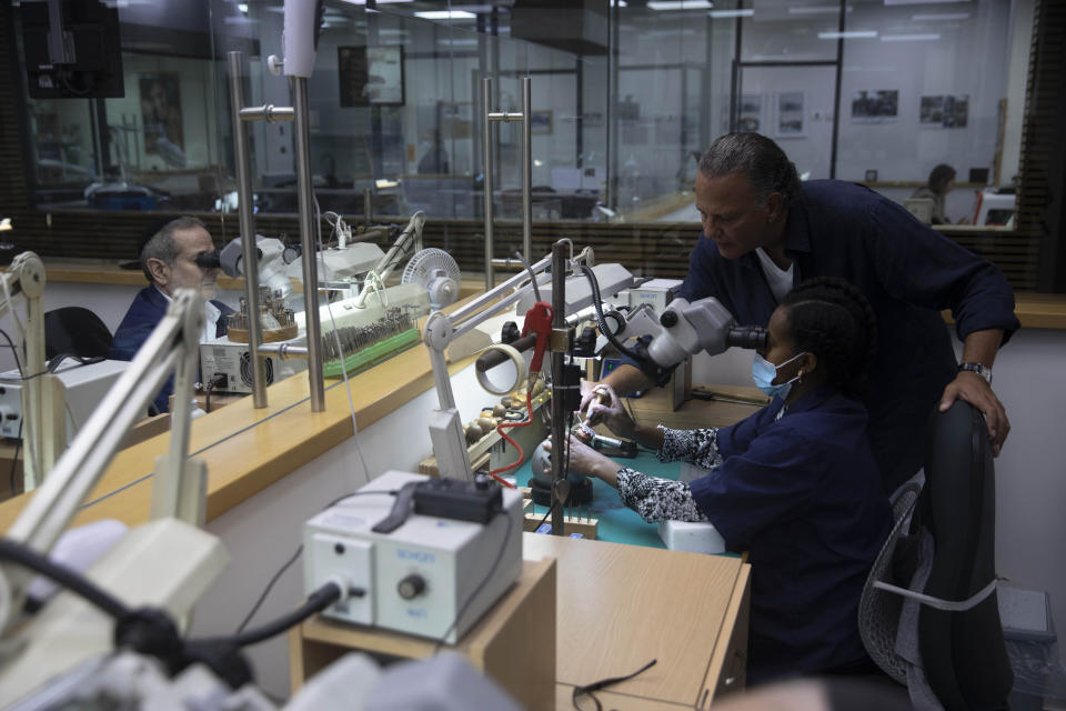 Isaac Levy, owner of Israeli jewelry company Yvel looks at a worker and parts of a mask in Motza near Jerusalem, Sunday, Aug. 9, 2020. An Israeli jewelry company is working on what it says will be the world's most expensive coronavirus mask, a gold, diamond-encrusted face covering with a price tag of $1. 5 million. (AP Photo/Sebastian Scheiner)