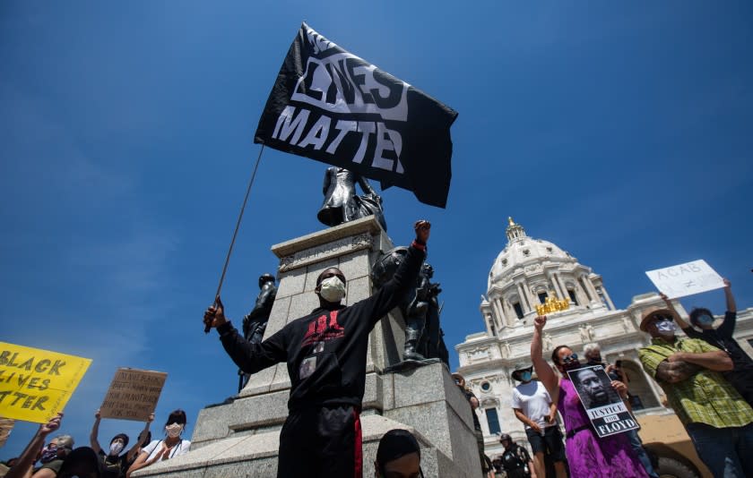 MINNEAPOLIS , MINNESOTA - MAY 31: A demonstrator stand on the steps of the Minnesota State waving a Black Lives Matters flag as thousands of protesters gather on Sunday to demand justice for George Floyd as the Minnesota National Guard secure the perimeter of the capitol building on Sunday, May 31, 2020 in Minneapolis , Minnesota. People want justice for the death of George Floyd by a police officer. (Jason Armond / Los Angeles Times)