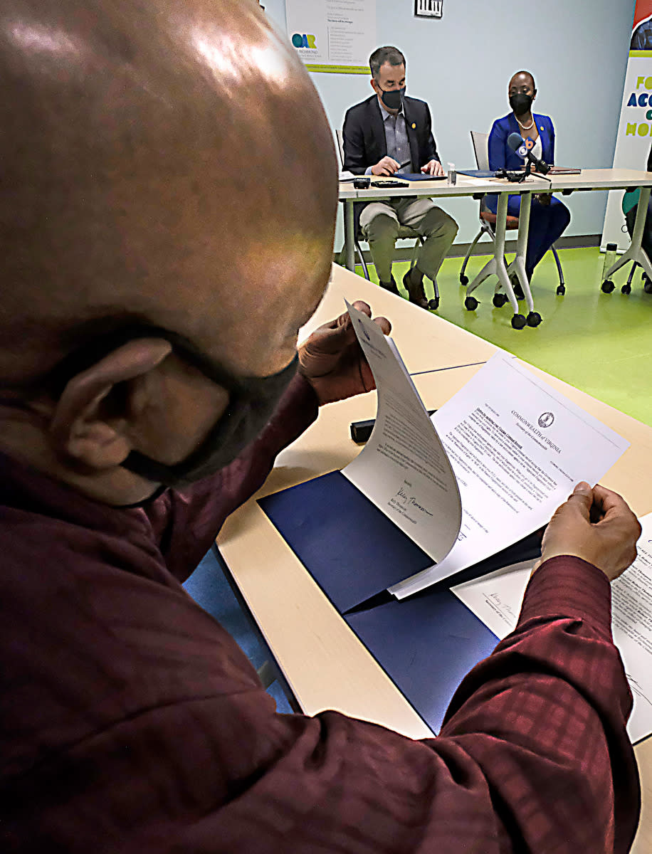 Robert Thompson looks at the restoration of rights document just signed by Virginia Governor Ralph Northam, center, in a ceremony at OAR of Richmond in Richmond, Va. Tuesday, March 16, 2021. On the right is Traci Deshazor, Deputy Secretary of the Commonwealth. (Bob Brown/Richmond Times-Dispatch via AP)