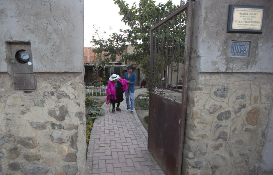 In this Aug. 23, 2018 photo, great-grandniece Rosa Lucas helps her 117-year-old aunt Julia Flores Colque go for a walk outside her home in Sacaba, Bolivia. The Sacaba mayor's office has named Flores Colque a living heritage. The office and a private foundation have improved her home, building the brick path where she walks, and a shower and toilet with a railing so the centenarian can safely make her way to the bathroom at night. (AP Photo/Juan Karita)