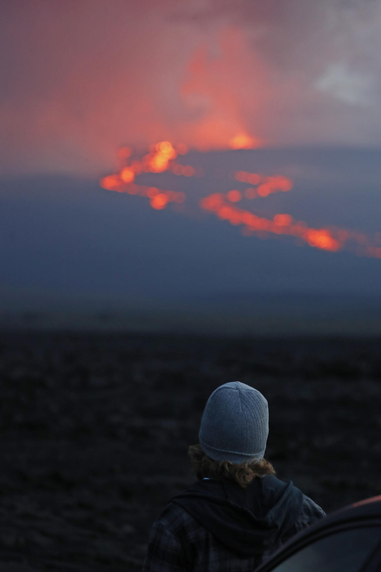 A spectator watches the lava flow down the mountain from the Mauna Loa eruption, Tuesday, Nov. 29, 2022, near Hilo, Hawaii. (AP Photo/Marco Garcia)