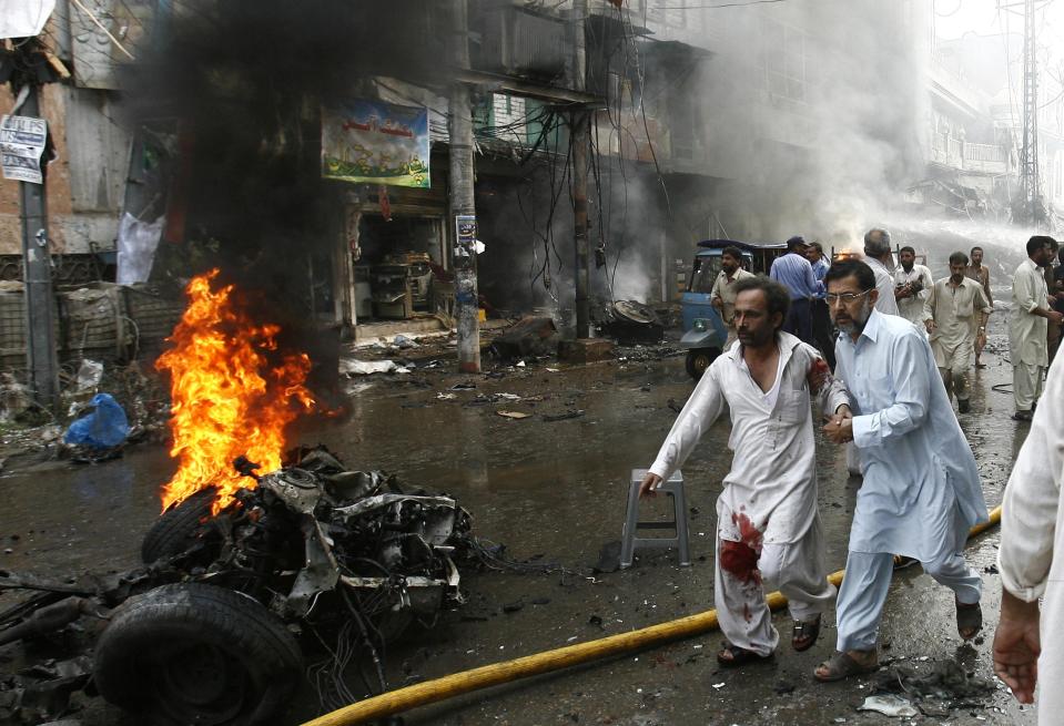 Man helps injured man walk away from the site of a bomb attack in Peshawar