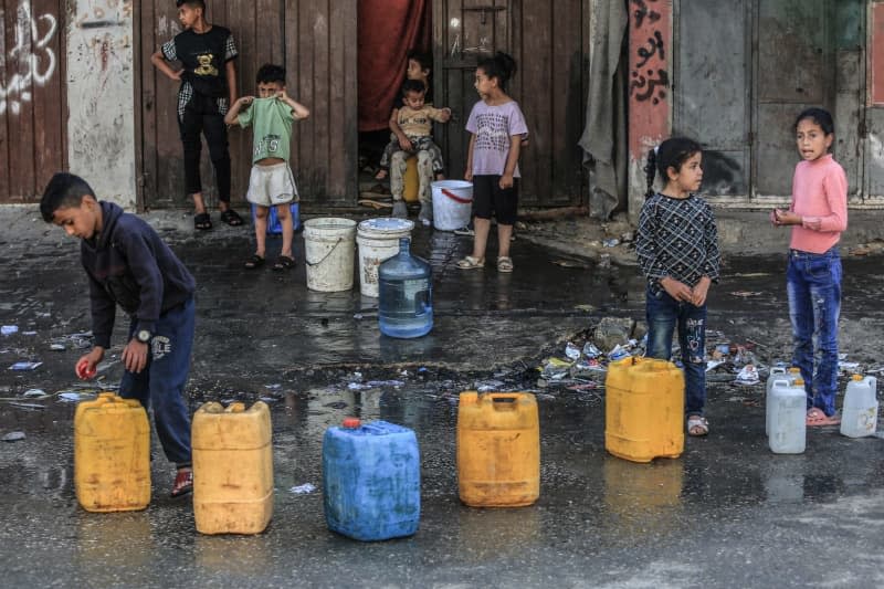 Palestinians children queue with water containers to fill them with drinking water. Palestinians are suffering from obtaining clean water due to the destruction of water wells during the battles between Israel and Hamas. Abed Rahim Khatib/dpa