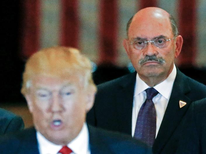 Allen Weisselberg looking at Trump and standing behind him at a news conference, with a US flag visible in the background.