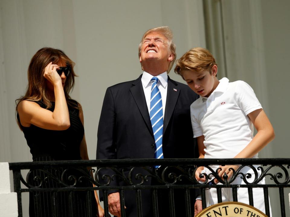 donald trump looking up at the sun squinting beside melania and barron trump in front of white house