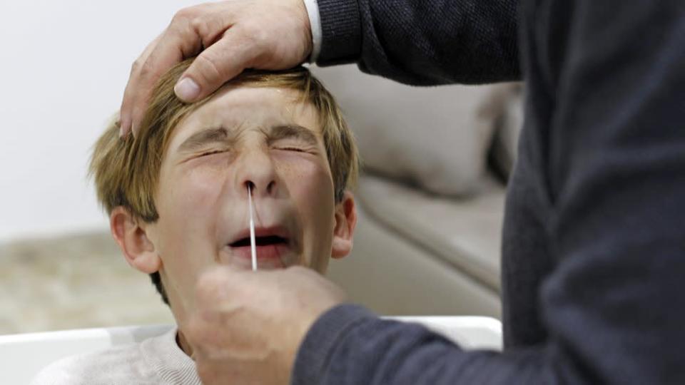 Un niño aprieta los ojos cuando le hurgan la nariz para una prueba de covid
