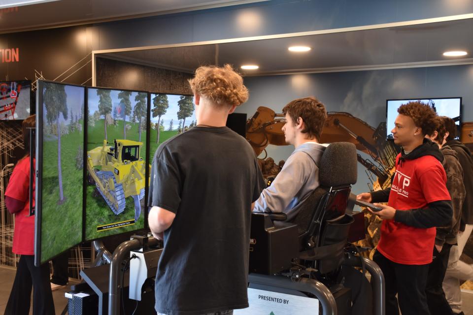 Gallatin High School students watch as their classmate drives an excavator simulator.