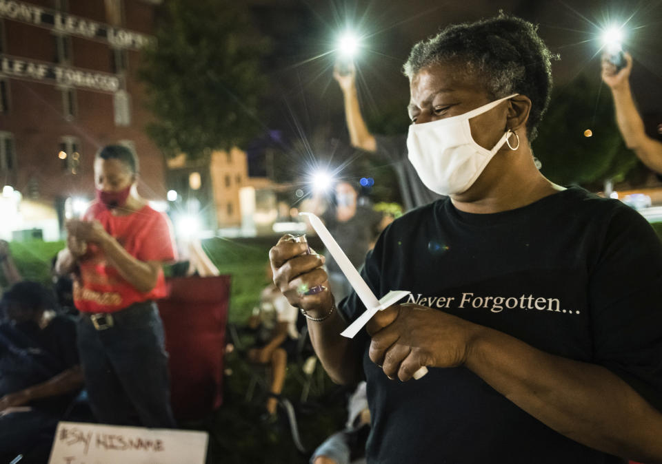 Janice Jordan, one of John Neville's aunts, lights a candle during a vigil for Neville on Wednesday, Aug. 5, 2020, in Bailey Park in Winston-Salem, N.C. Demonstrators held the vigil to demand justice for Neville, a Black man who died days after his December 2019 arrest following the release of body camera videos that showed him struggling with guards and yelling he couldn’t breathe as they restrained him. (Allison Lee Isley/The Winston-Salem Journal via AP)