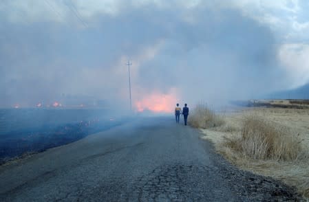 Iraqi men walk near a fire from a wheat field on the outskirts of Mosul