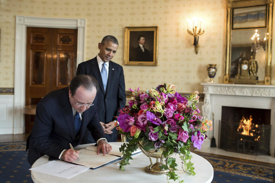 In this Feb. 11, 2014 photo provided by Stichting Kunstboek, French President François Hollande signs the guest book as President Obama looks on at the White House in Washington. For the state visit, a centerpiece bouquet of early spring flowers in the French style is presented in a gilded pedestal Vermeil vase, part of the historic White House collection. The gloriosa lilies mimic the flames of the fire in the Blue Room. The photograph is featured in the book "Floral Diplomacy: At the White House," by Laura Dowling. (Pete Souza/The White House/Stichting Kunstboek via AP)
