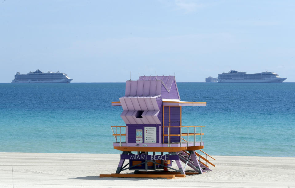 Two cruise ships are anchored offshore past a lifeguard tower, Tuesday, March 31, 2020, in Miami Beach, Fla. (AP Photo/Wilfredo Lee)