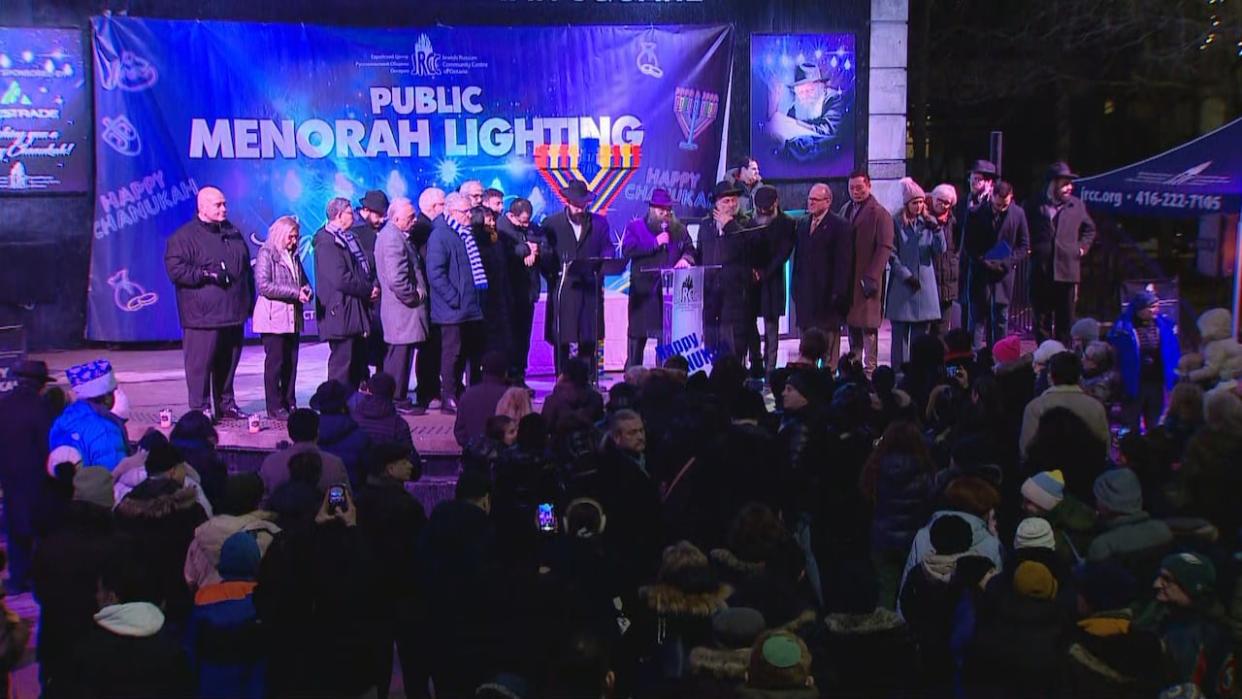 A number of political leaders, including Toronto Mayor Olivia Chow and Vaughan Mayor Steven Del Duca, gather on stage at Mel Lastman Square as part of a public menorah lighting on Thursday. (CBC - image credit)