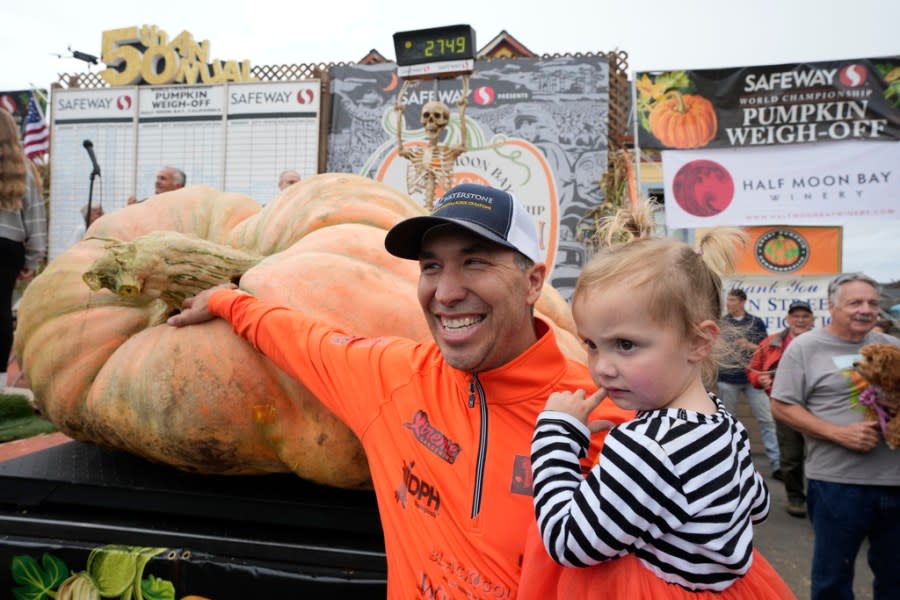 Travis Gienger of Anoka, Minn., holds his two-year-old daughter Lily and poses by his pumpkin called “Michael Jordan” after winning the Safeway 50th annual World Championship Pumpkin Weigh-Off in Half Moon Bay, Calif., Monday, Oct. 9, 2023. Gienger won the event with a pumpkin weighing 2749 pounds. (AP Photo/Eric Risberg)