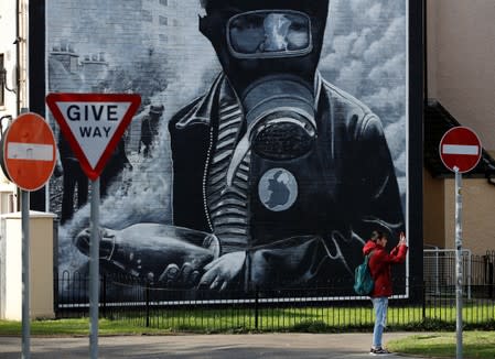 A man takes a photograph of a mural in the Bogside area of Londonderry, Northern Ireland