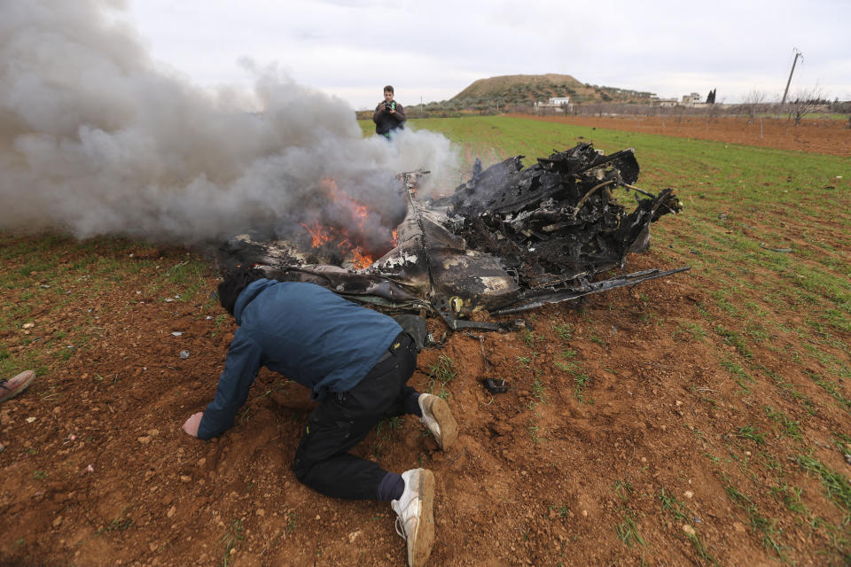 Rebel fighters look at a Syrian government helicopter that was shot down in Idlib province, Syria, Tuesday, Feb. 11, 2020. Syrian rebels shot down a government helicopter Tuesday in the country's northwest where Syrian troops are on the offensive in the last rebel stronghold. (AP Photo/Ghaith Alsayed)