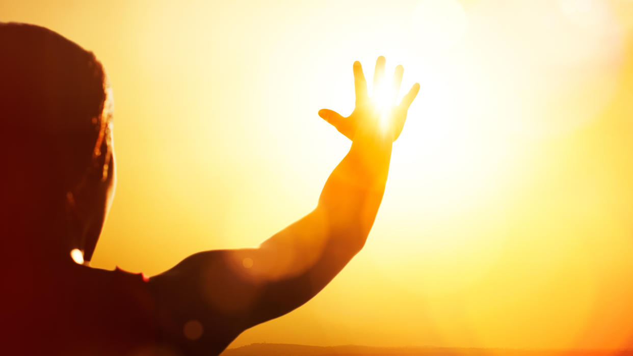  Young woman shown in silhouette as she's reaching for the sun. 