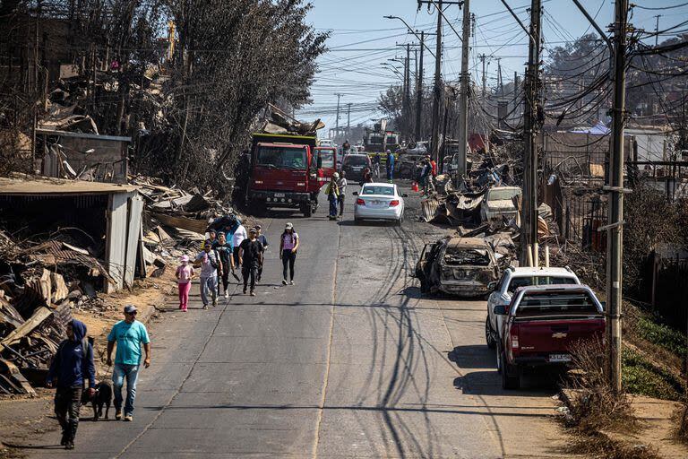 Personas caminan frente a casas y restos de automóviles destruidos por un incendio forestal, en Viña del Mar, Chile, el 5 de febrero de 2024. (Xinhua/Str) 