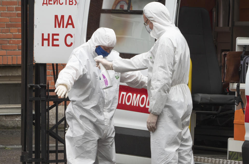 A medical worker wearing protective equipment disinfects his colleague after escorting a patient by ambulance to a hospital for COVID-19 patients in St. Petersburg, Russia, Monday, May 18, 2020. (AP Photo/Dmitri Lovetsky)