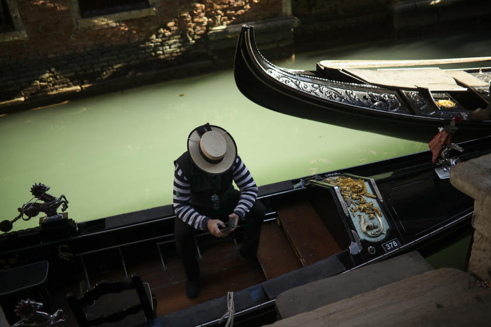 FILE - In this Friday, Feb. 28, 2020 file photo, a gondolier looks at his smartphone as he waits for clients in Venice, Italy. The European Union on Wednesday, May 19, 2021 took a step toward relaxing tourism travel for visitors from outside the bloc, with EU ambassadors agreeing on measures to allow fully vaccinated visitors in. They also agreed on easing the criteria for nations to be considered a safe country, from which all tourists can travel. Up to now, that list included only seven nations. (AP Photo/Francisco Seco, File)