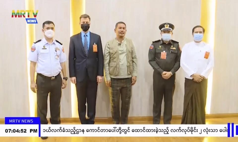 In this image taken from video by Myanmar state broadcaster MRTV, American Kyaw Htay Oo, center, poses with unidentified officials at the Yangon International Airport in Yangon, Myanmar on Thursday, Nov. 17, 2022. Myanmar’s military-controlled government says it is releasing and deporting an Australian academic, a Japanese filmmaker, an ex-British diplomat and an American as part of a broad prisoner amnesty marking the country’s National Victory Day. (MRTV via AP)