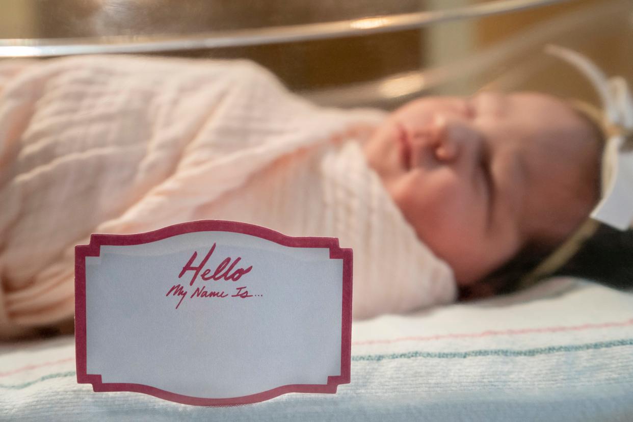 Newborn baby sleeping in hospital bed with name tag on the crib blank.