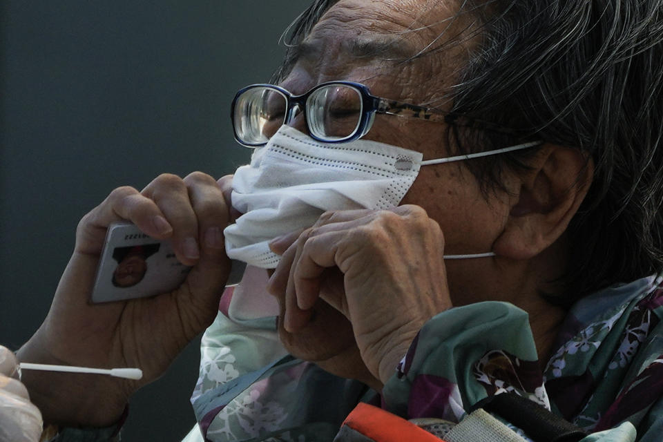 A woman pulls up her mask to get her routine COVID-19 throat swab at a coronavirus testing site in Beijing, Monday, Sept. 5, 2022. (AP Photo/Andy Wong)