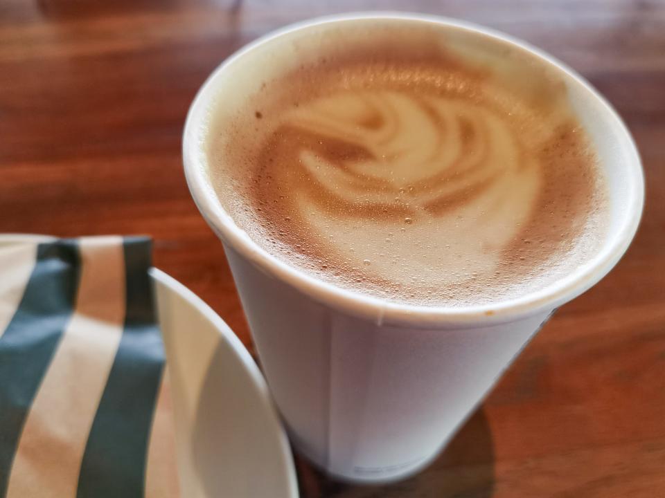 cappuccino drink from starbucks with foam art on time next to a pastry bag from starbucks