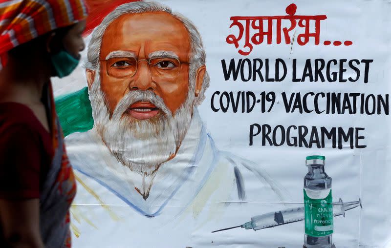 FILE PHOTO: A woman walks past a painting of Indian Prime Minister Narendra Modi a day before the inauguration of the COVID-19 vaccination drive on a street in Mumbai