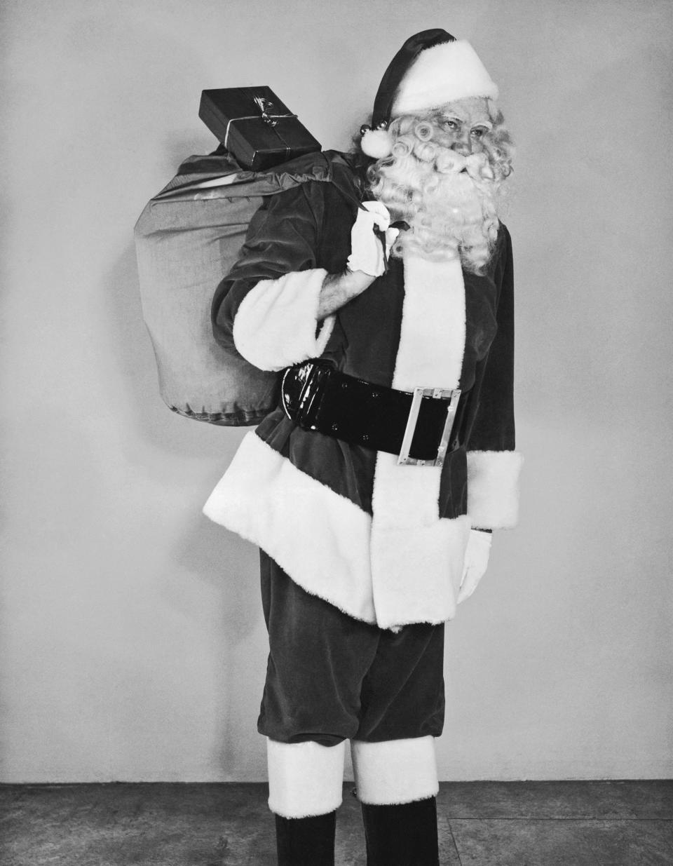 Santa Claus carrying a bag full of presents in the late 1940s.