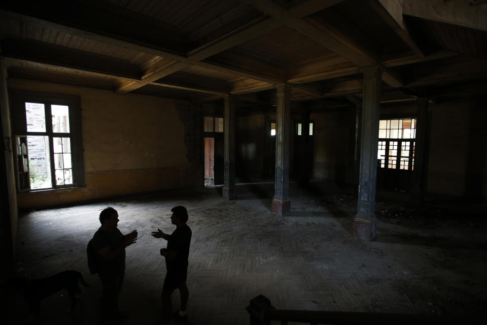 In this Saturday, July 21, 2018 photo, Erol Baytas, 56, the caretaker of the 6-floor timber building that once served as an orphanage for children of the minority Greek community, talks to Korhan Gomus, 64, left, an architect and urban planning professor, in Buyukada, the largest and most popular of the Princes' Islands in the Sea of Marmara near Istanbul. The 120-year-old gigantic Prinkipo orphanage, occupying 20,000 square meters on a hilltop_ became home for some 5,800 minority Greek children from 1903 until 1964 when it was forced to shut down. (AP Photo/Lefteris Pitarakis)