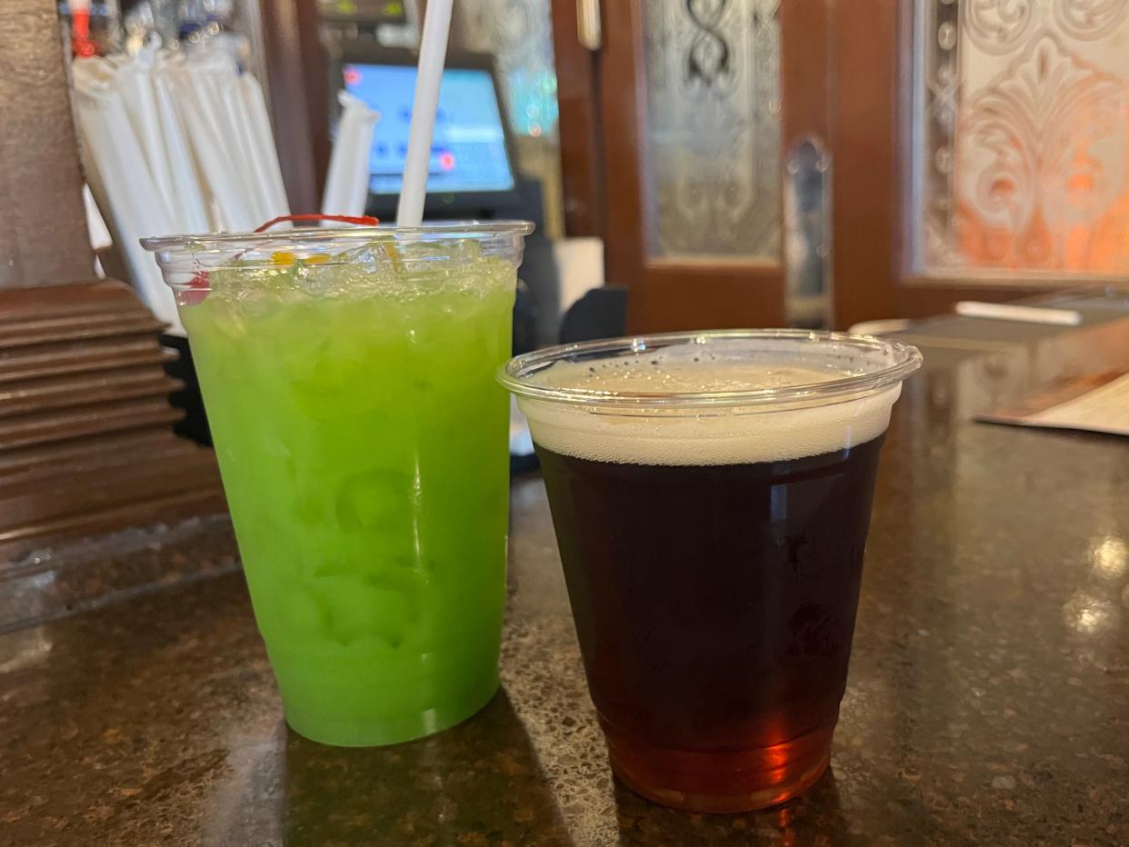 a green cocktail and a beer in plastic cups on the bar at rose and crown in epcot