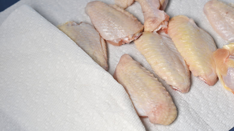 Chicken wings being dried between sheets of paper towel