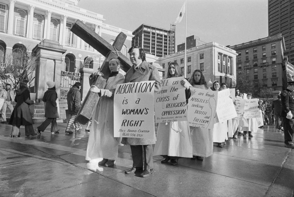 Protesters carry a cross and signs reading "abortion is a woman's right" and "free us from the cross of religious oppression"