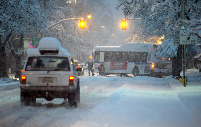 Lane Transit District workers try to free a bus stuck on 11th Street in Eugene, Ore., early Monday, February 25, 2019 after several inches of snow fell in area. Schools, including the University of Oregon were closed. (Andy Nelson/The Register-Guard via AP)